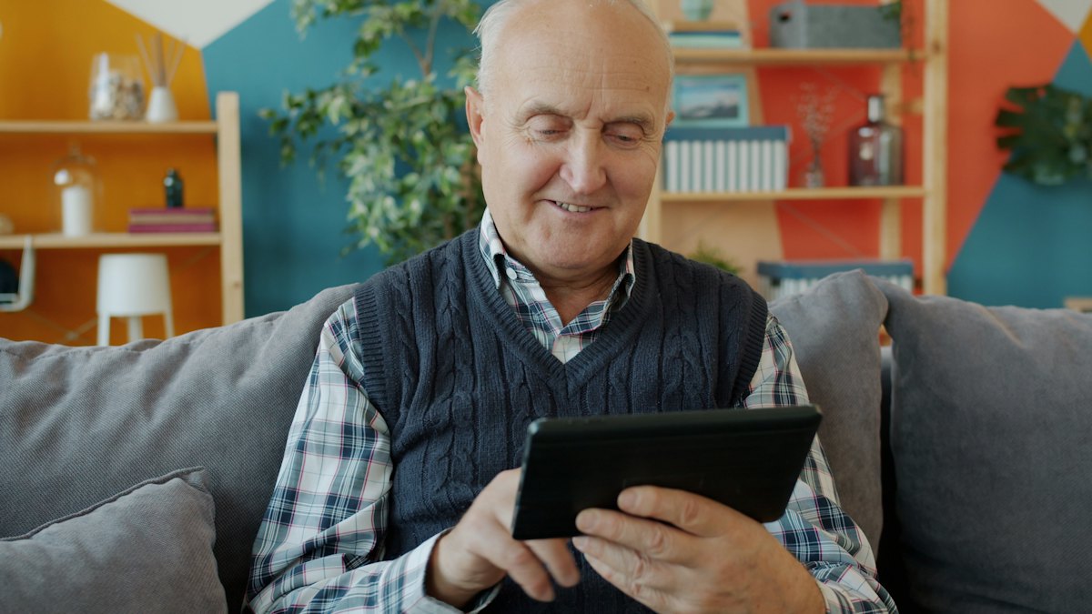 Un retraité souriant utilise une tablette dans son salon